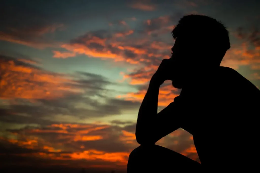 Silhouette of a person sitting thoughtfully against a vibrant sunset sky, symbolizing emotional reflection and solitude.